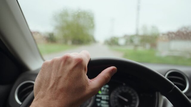 Close-up view of a driver's hand gripping a steering wheel from the cockpit, emphasizing control and motion as the car moves down the street, conveying commute and travel, 4K