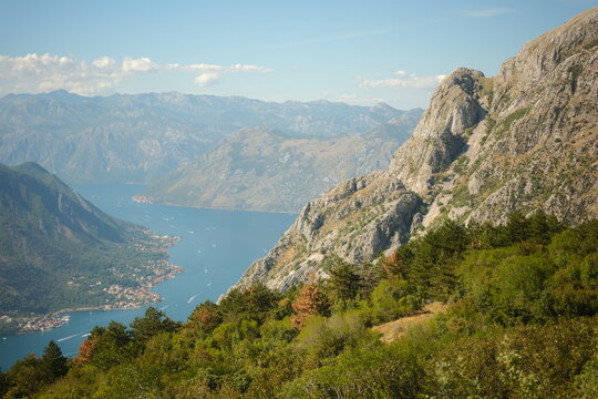 Panoramic view of the Bay of Kotor (Boka Kotorska) in Montenegro. Scenic coastal landscape with deep blue sea, majestic mountains, and a small town at the foot of the cliffs.