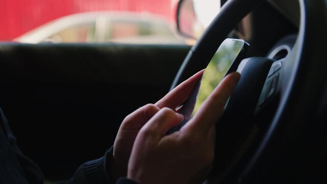 Close-up of female hands holding a smartphone at a car steering wheel, illustrating distracted driving, mobile phone use and road safety risks in everyday commuting situations. 4K.