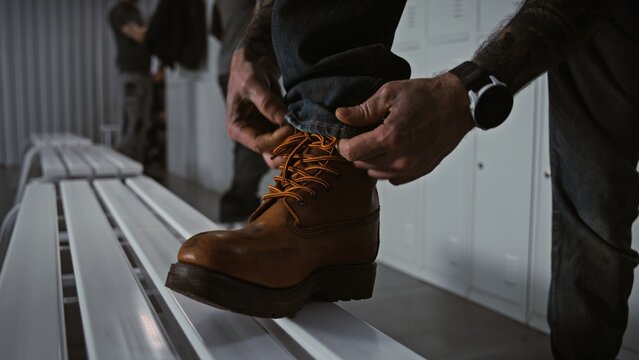 Close Up of Manual Laborer Resting Foot on Metal Bench, Carefully Tying Laces of Sturdy Protective Boots in Modern Warehouse or Factory Dressing Area. Concept of Industrial Gear and Readiness.