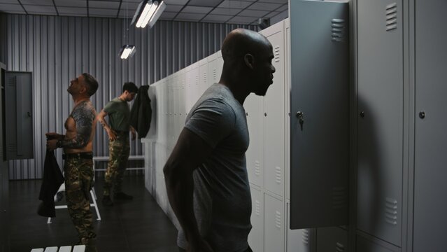 Group of Diverse Soldiers in Tactical Camouflage Interact in Locker Room, Some Undressing After Mission While Others Put On Gear For Next Watch. Concept of Army Workplace Routine and Shift Handover.