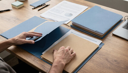 Organized workspace with hands opening a blue folder and documents spread © Екатерина Чумаченко