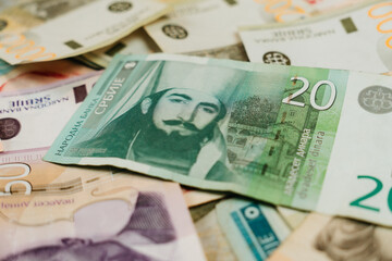 Obraz premium A twenty Serbian dinar banknote lies over scattered Serbian cash on the table. Small denomination currency concept for local payment, retail pricing and everyday spending