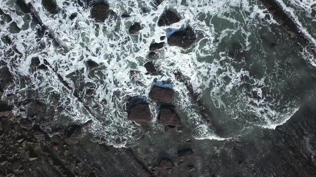 Dramatic aerial top down view showing powerful ocean waves crashing against the unique Sakoneta flysch rock formations along the rugged coastline of the Basque Country in northern Spain