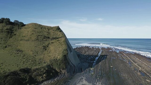 Aerial view moving forward showing the spectacular flysch rock formations on the Basque coast at Sakoneta beach, near Zumaia, revealing the rugged beauty of the coastline under a clear blue sky