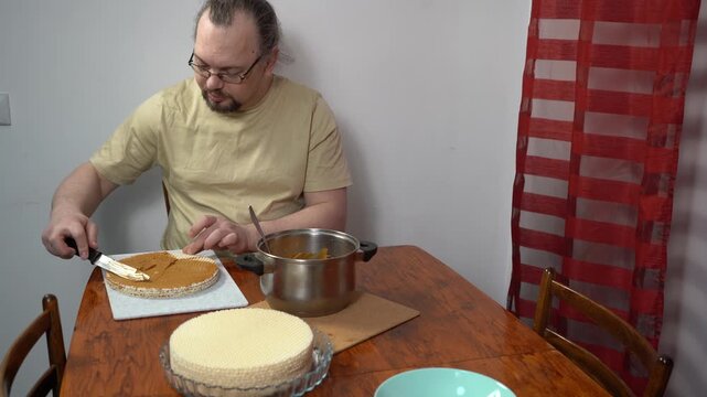 Spread cream on the cakes. Man is making a waffle cake with condensed milk. Sweet food