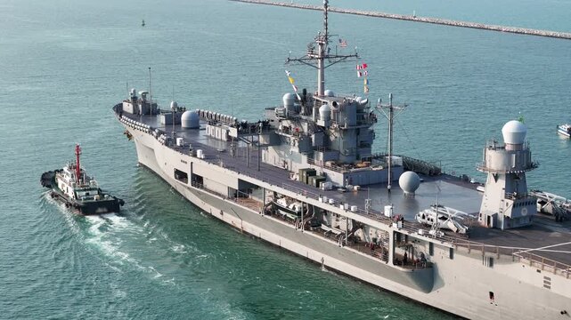 large naval amphibious assault ship being assisted by tugboats in the strategic Strait of Hormuz. Concept of maritime security, naval power projection, and protection of international shipping lanes.