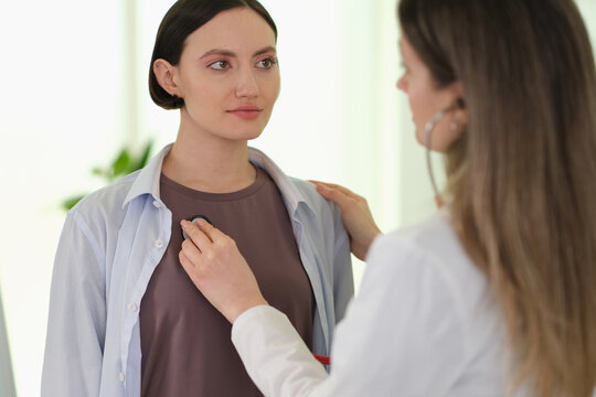Doctor performing chest auscultation during routine exam patient seated, stethoscope placed on shirt, clinician checking lungs