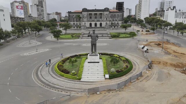 Drone hovers in wide shot of Independence Square with statue of Samora Machel, city hall, and a white cathedral on an overcast day in Maputo, Mozambique