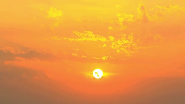 Vibrant orange sunset with bright sun and scattered clouds in the sky