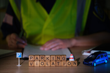 Obraz premium A traffic enforcement officer sits at a desk, writing down parking violations. Wooden blocks spell out PARKING VIOLATION, beside a small traffic cone and a toy car, creating a serious atmosphere.