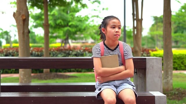Cute Asian student girl with backpack sitting on a bench and waiting for the bus, Back to school concept.
