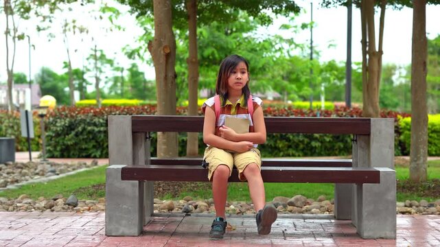 Cute Asian student girl with backpack sitting on a bench and waiting for the bus, Back to school concept.