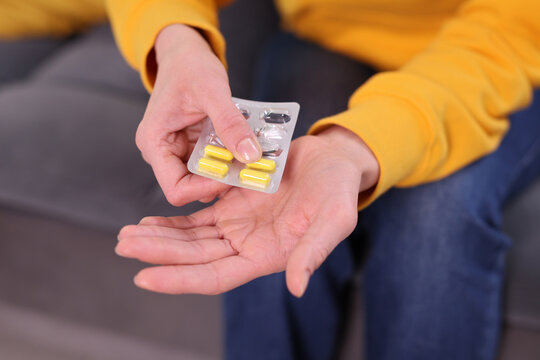 A person sits on a soft couch, holding a packet of vitamins. They carefully pour colorful capsules into their palm while wearing a bright yellow sweater and casual blue jeans.