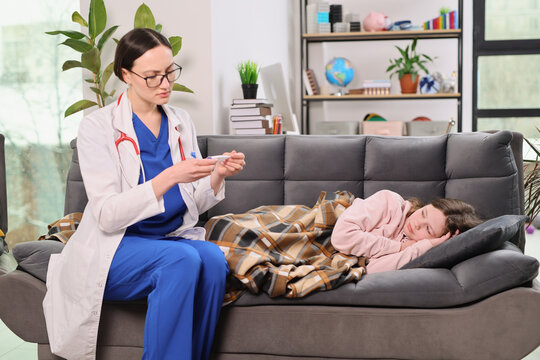 A dedicated doctor in a white coat sits beside a young girl wrapped in a warm blanket. They are in a comfortable living room with a casual and nurturing atmosphere.