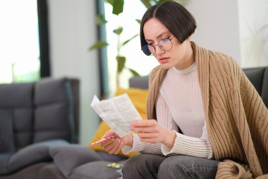 A woman sits comfortably in a stylish living room, wrapped in a warm sweater. She intently reads a newspaper, surrounded by greenery and soft furnishings, enjoying a peaceful moment.