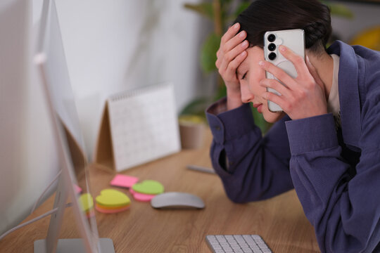 A young professional appears distressed while talking on the phone in a modern office. Their workspace shows sticky notes and a calendar, capturing the hectic atmosphere of the day.