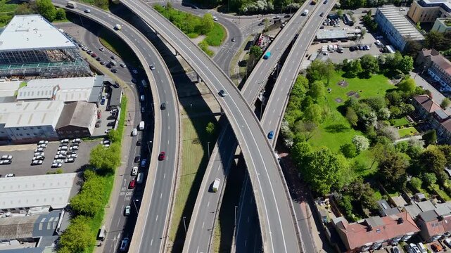 rone shot of a complex motorway junction with multiple curved lanes and flowing traffic surrounded by suburban buildings and greenery.