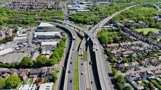 Top-down aerial perspective of a large highway interchange with continuous vehicle movement and surrounding urban and green landscape.