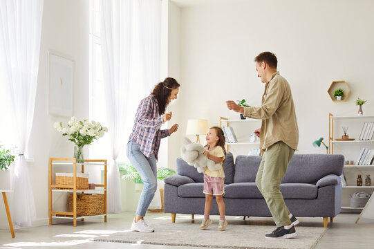 Family with daughter dancing happily at home. Smiling parents guide child having fun in a cozy interior, bonding. The cheerful girl laughs while they play together. Concept happy family time.