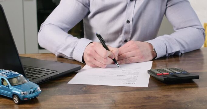 Male agent fills out car insurance policy and counts on calculator at desk closeup. Specialist determines total amount of agreement payment for client in office