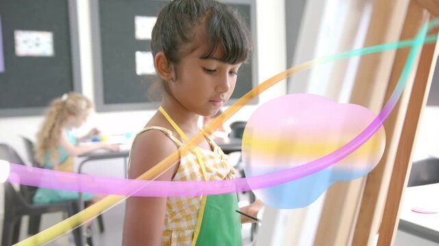 Girl painting at easel in classroom, ribbons sweeping revealing face and palette while practicing