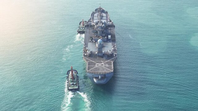 large naval amphibious assault ship being assisted by tugboats in the strategic Strait of Hormuz. Concept of maritime security, naval power projection, and protection of international shipping lanes.