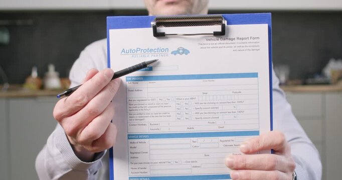 Man holds vehicle report form on clipboard pointing at printed lines with pen. Driver presents claim details guiding document review for car insurance process slow motion