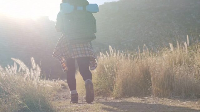 Female hiker walking trail, camera pulling back while sun showing backpack rolled pad, travel