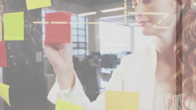 Woman selecting yellow sticky note, placing and writing on glass with marker for marketing