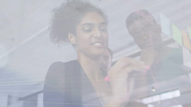 Woman picking up pink marker sketching business plan on clear glass panel while colleagues nodding