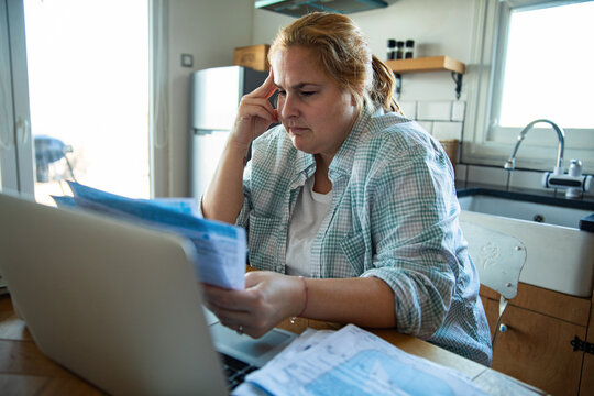 Stressed woman reviewing household bills at home kitchen table