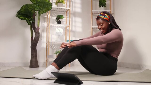 African woman exercising at home following an online yoga stretching session