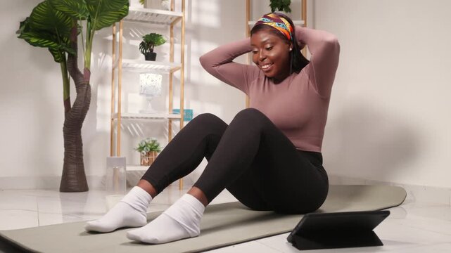 African woman doing happy fitness workout on a yoga mat in her bright home