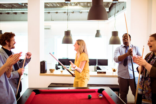 Coworkers playing pool in modern office break room
