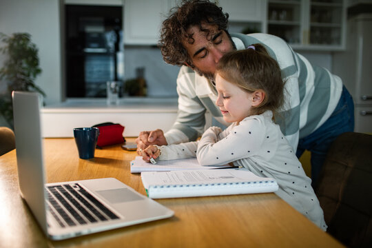 Father helping daughter with homework at kitchen table