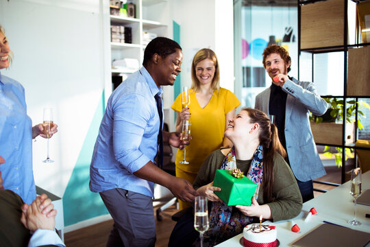 Coworkers celebrating birthday with gift in modern office