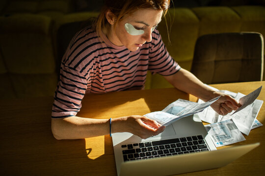Woman paying bills at home on laptop with under-eye patches