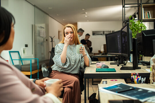 Two female colleagues chatting during coffee break in modern open plan office