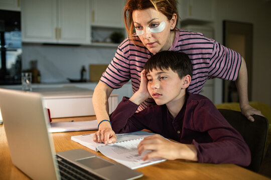 Tired mother helping bored son with homework at kitchen table