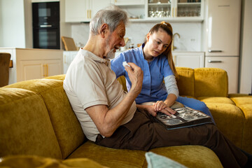Obraz premium Caregiver comforting senior man while looking at a photo album at home