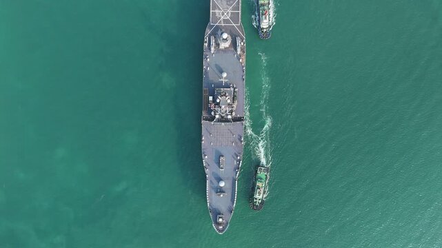 large naval amphibious assault ship being assisted by tugboats in the strategic Strait of Hormuz. Concept of maritime security, naval power projection, and protection of international shipping lanes.