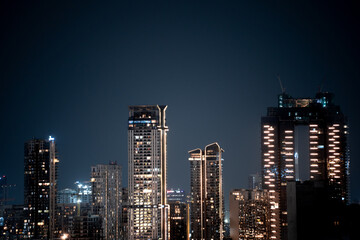 Fototapeta premium Modern highrise multi storey skyscrapers at night with lights shining through showcasing growth of apartments, buildings, houses and shopping centers in cities like gurgaon, delhi, bangalore, hyderaba