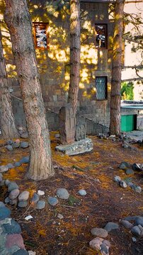 Vertical shot of a traditional stone cross khachkar near the Kecharis Monastery walls surrounded by tall pine trees in Tsaghkadzor, Armenia.