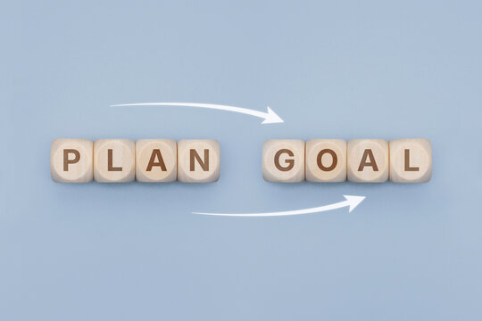 Wooden blocks forming words PLAN and GOAL connected by white arrows on a light blue surface. Concept project management workflow, strategic planning, achieving targets and coaching.