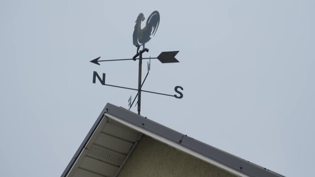 Weather vane on a roof shows directions from north to south in a cloudy sky