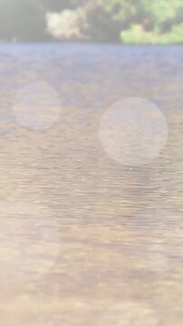 Vertical video: After flare appearing, camera moving closer and revealing rippling sunlit lake