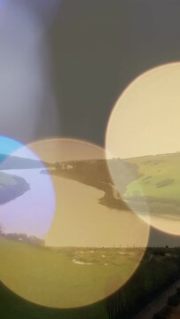 Vertical video: Color bokeh discs appearing sliding mixing and fading revealing river bend and road