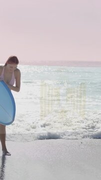Vertical video: Surfer holding blue board walking onto wet sand as waves receding ending surf ride