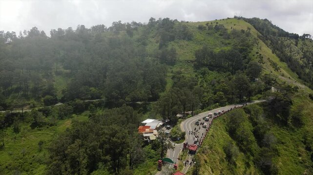 4K aerial view of Bromo volcanic valley, winding roads, and tourists at a scenic mountain viewpoint.